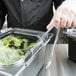 A person wearing a plastic glove using a Carlisle clear plastic food pan lid to cover a container of food.