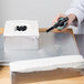 A person using a Matfer Bourgeat square cake frame to cut a cake.