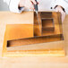 A hand using a Matfer Bourgeat metal cake cutter to cut a cake on a table.