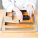 A chef using a Matfer Bourgeat wedding cake frame to cut a cake on a tray.