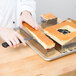 A hand using a Matfer Bourgeat French style cake frame to cut a square piece of cake.