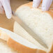 A person in gloves uses a Mercer Culinary Renaissance forged tomato knife to cut a piece of bread.