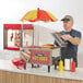 A small countertop hot dog cart with a red and yellow umbrella, labeled 'Tasty Hot Dogs,' designed for holding and serving hot dogs and buns.