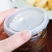 A person holding a white plastic Cambro lid with a straw slot on a jar of liquid.