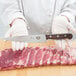 A person using a Victorinox serrated edge chef knife with a rosewood handle to cut meat.