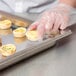 A person in plastic gloves putting food in a Vollrath stainless steel steam table pan.