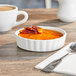 An Acopa round white bowl filled with food on a table with a spoon next to it.