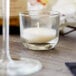 A Sterno PetiteLites clear wax candle in a glass on a table with a glass of liquid.