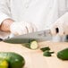 A person using a Mercer Culinary Z&#252;M&#174; chef knife to cut a cucumber on a counter.