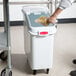 A person's arm using a handle to put food into a white Rubbermaid ingredient container.