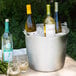 A Vollrath stainless steel utility bucket filled with white wine and glasses on a table.