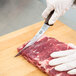 A person wearing a glove with a wooden-handled Victorinox curved boning knife cutting meat on a counter.