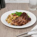 A Reserve by Libbey bone china dinner plate with meat and vegetables on it on a table with a knife and fork.