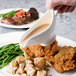 A person pouring gravy into a Reserve by Libbey bone china sauce boat on a plate of food.