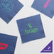 A group of navy blue Choice beverage napkins with customizable green and pink logos.