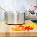 A person stirring food in a Vollrath Wear-Ever sauce pan.