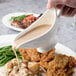 A person pouring gravy into a white gravy boat.