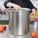 A person holding a silver Vollrath pot lid over a large pot.