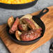 An Elite Global Solutions faux cast iron fry pan with potatoes and herbs on a table.