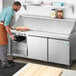 An aproned man using an Avantco stainless steel sandwich prep table.