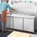 A man in an apron using an Avantco stainless steel sandwich prep table to make a sandwich.