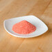 A small white plate with a pile of red salt on it.