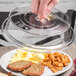 A person holding a Cambro clear low profile plate cover over a plate of food.