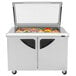 A Turbo Air stainless steel refrigerated sandwich prep table with glass lids over food trays.