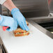 A person in blue gloves cutting a sandwich on an Avantco refrigerated sandwich prep table.