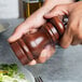 A person using a Fletchers' Mill walnut stain wooden pepper mill on a plate of food.