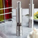 A Fletchers' Mill stainless steel and acrylic pepper mill on a table with a black pepper in it.