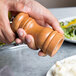 A hand holding a Fletchers' Mill cherry wooden salt mill over a plate of food.