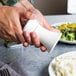 A person holding a white Fletchers' Mill Sierra salt mill over a plate of food.