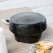 A black Dinex soup bowl lid on a table with a spoon and cookies.