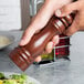 A close-up of a person holding a Fletchers' Mill walnut stain wooden pepper mill.