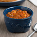 A dark blue Dinex insulated bowl filled with food on a table with a spoon.