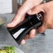 A person holding a Fletchers' Mill Sierra black pepper mill over a plate of food.