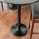 A black Lancaster Table & Seating cast iron table base with two black chairs on a wood floor.