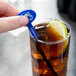 A person holding a blue plastic oval stirrer in a glass of brown liquid with a lime slice.