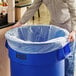 A man holding a Lavex blue garbage bag over a full trash can.