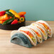 A row of tacos on a HS Inc. jalapeno shell taco server with cheese and vegetables.
