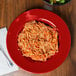 A GET cranberry melamine bowl with a plate of spaghetti and a bowl of salad on a table.