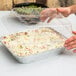 A person holding a tray of food with a foil lid.