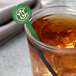 A clear cup of brown liquid with ice and a green WNA Comet disc stirrer in it.