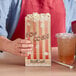 A hand holding a Bagcraft EcoCraft popcorn bag next to a plastic cup of drink.