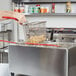 A hand holding a basket of fries in a Cecilware electric countertop deep fryer.