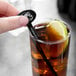 A person holding a black oval stirrer in a glass of brown liquid with a lime wedge.