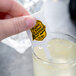 A hand using a white WNA Comet rectangular stirrer in a glass of lemonade.
