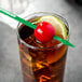 A green WNA Comet oval stirrer with a cherry and lime slice in a drink.