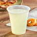 A Fabri-Kal Nexclear plastic cup filled with a drink on a table with a bag of onion rings.
